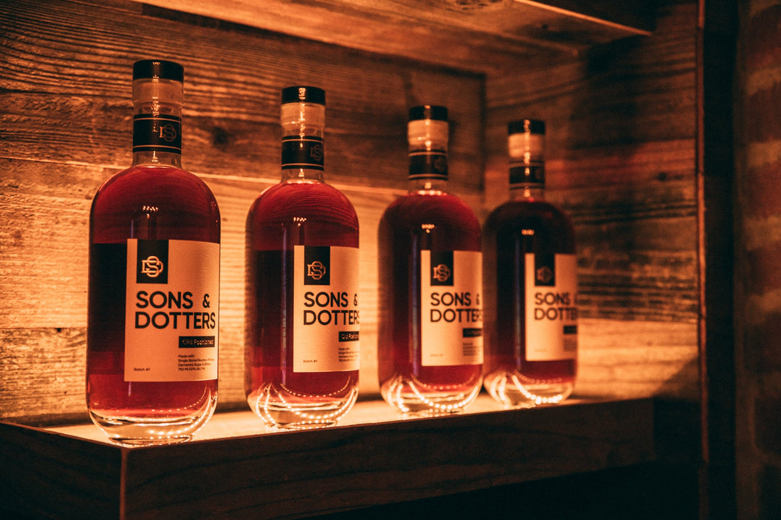 Sons & Dotters Old Fashioned bottles lined up behind a bar shelf — rich amber color, crafted in San Diego.