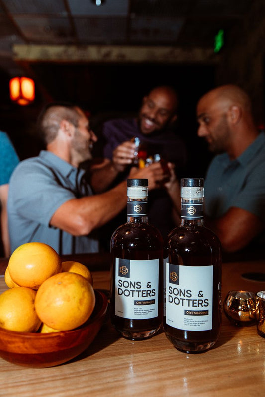  Friends raising Old Fashioneds at a holiday party, Sons & Dotters bottles in foreground.
