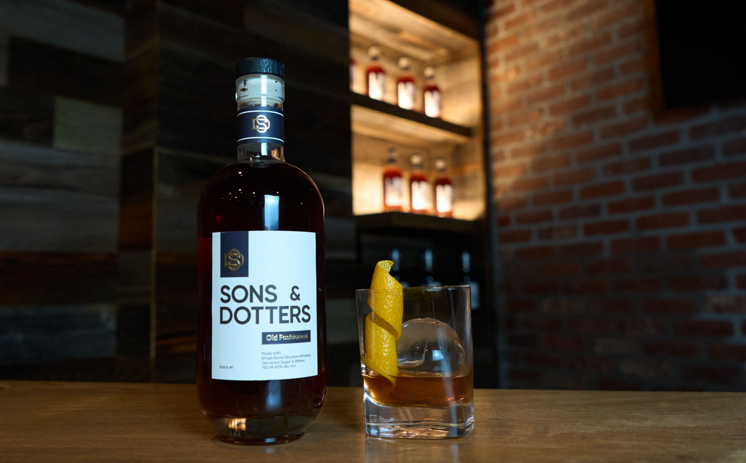 A bottle of Sons & Dotters sitting on a bar top next to a perfectly made Old Fashioned
