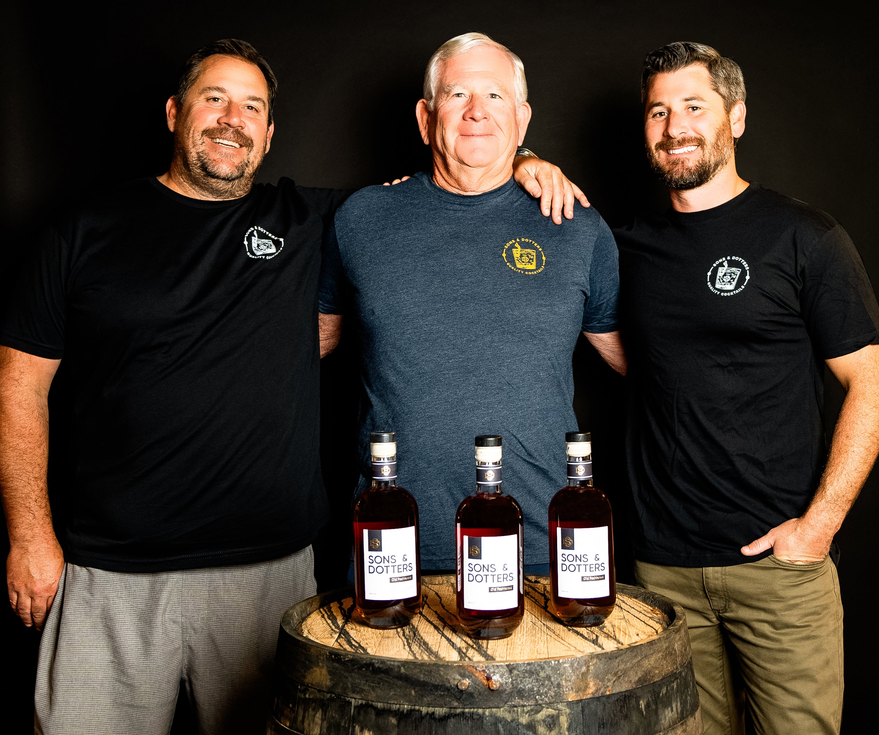 Three founders standing around a bourbon barrel with three bottles of Sons & Dotters on top of it